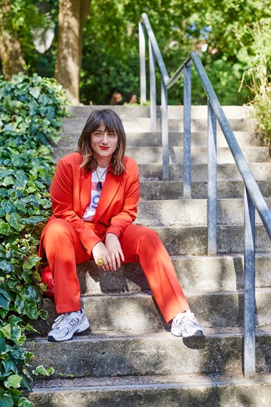 Headshot of women wearing a red suit, sitting on stairs